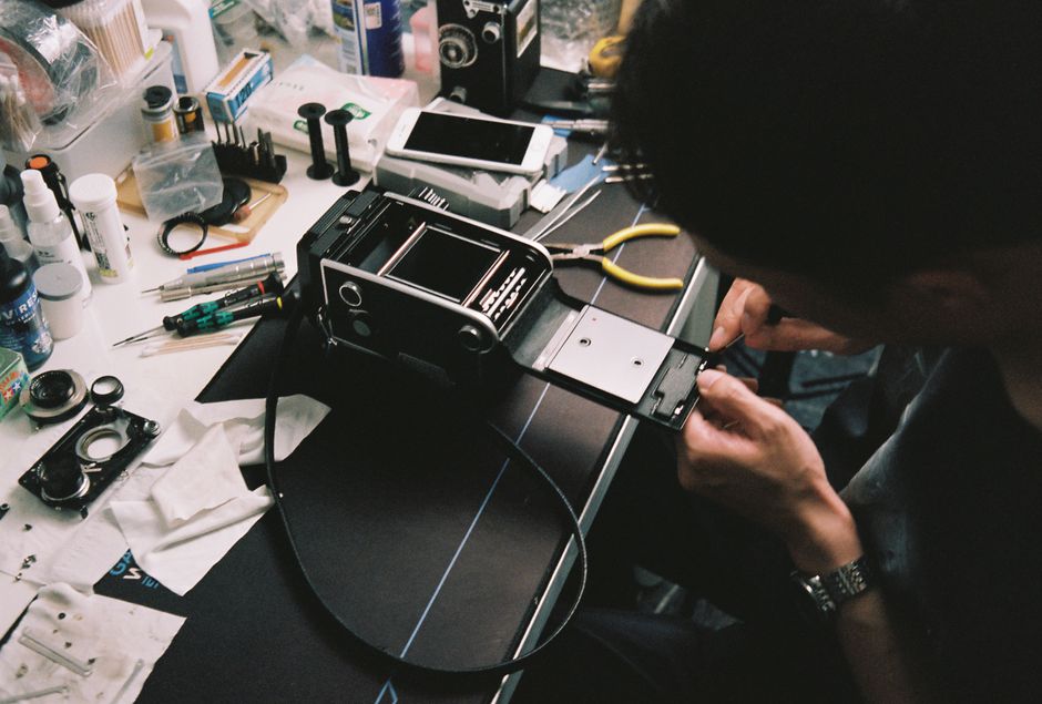 A man skillfully repairs a vintage camera in a cluttered workshop filled with tools.